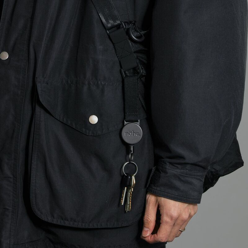 Zwarte Nähe uittrekbare Sleutelring Extension met sleutels, vastgeklikt aan een jastouwtje. Matte afwerking met reliëflogo.