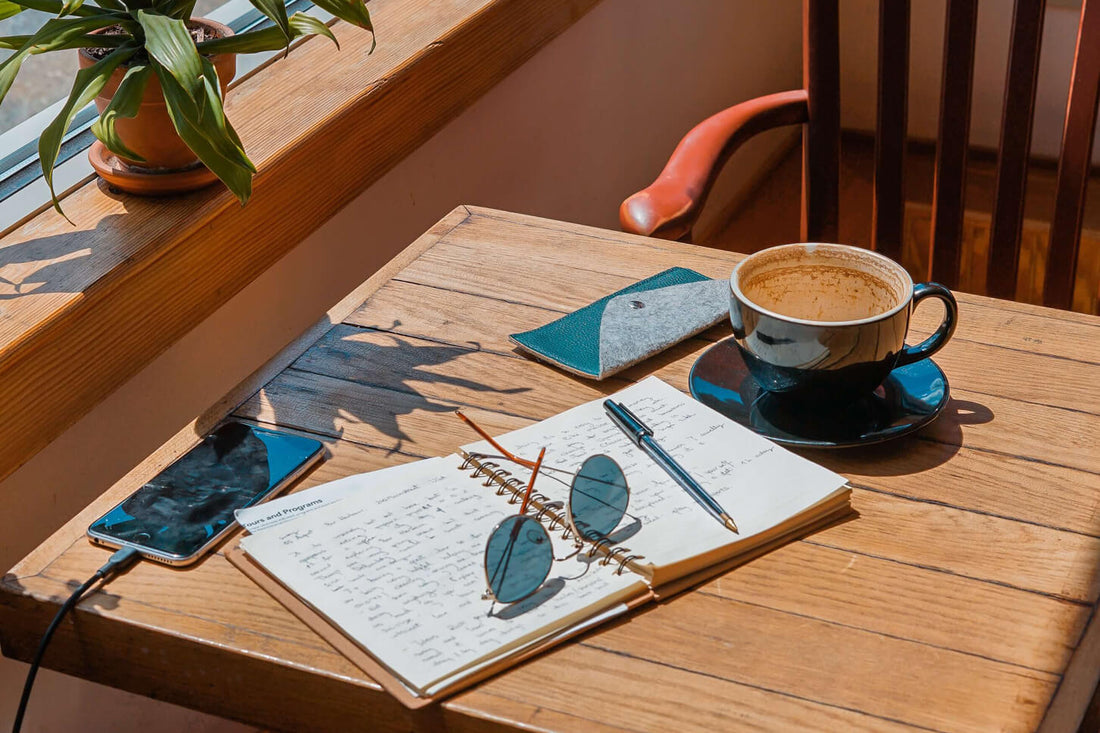 Een opengeslagen travel journal in de zon op een tafel in een cafe met een kop koffie en een zonnebril