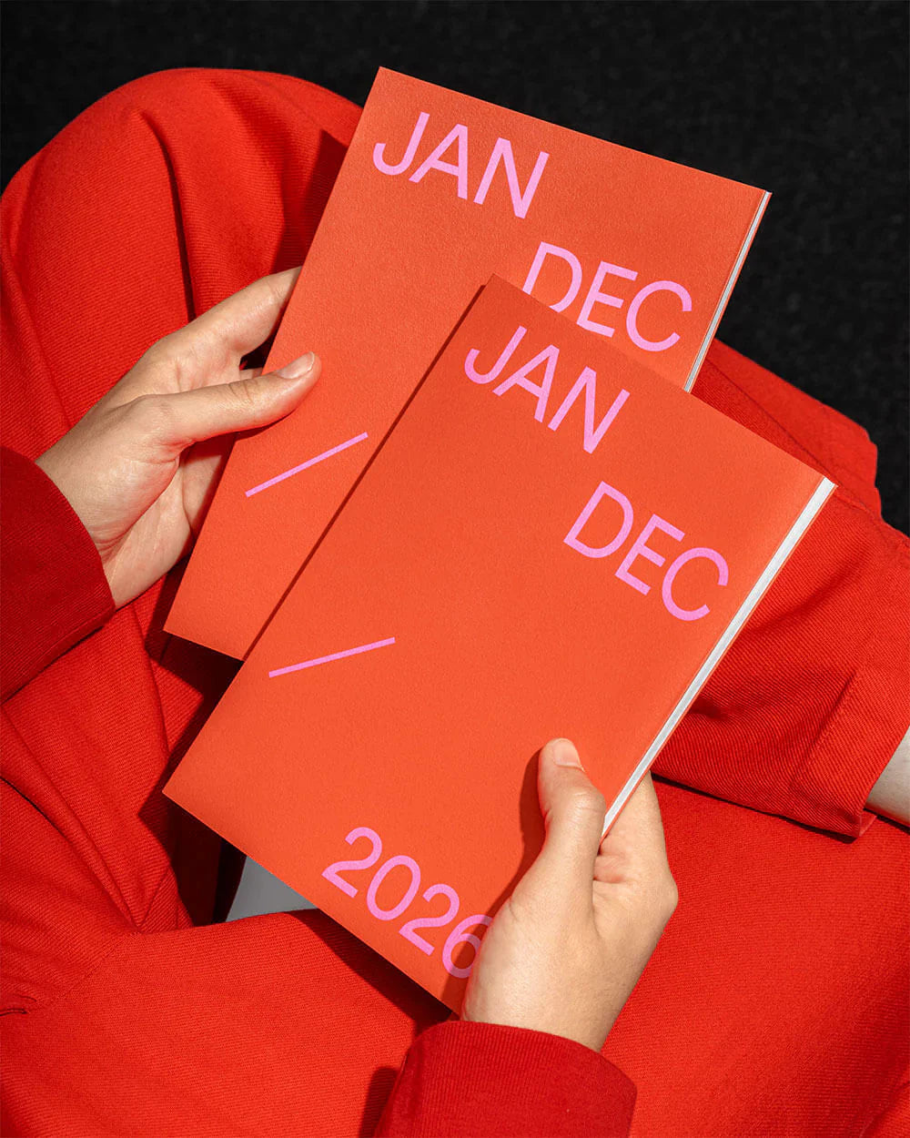 Persoon houdt twee 2026 agenda's vast in een felrode kleur met teksten voor januari en december.