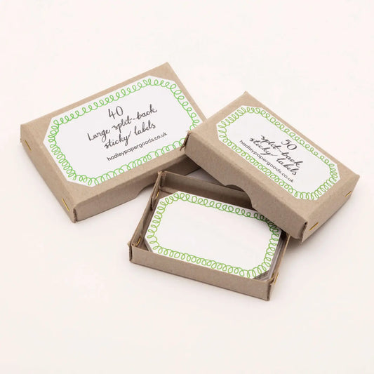 White rectangular sticky labels with a green looped border design in small brown kraft paper boxes by Hadley.