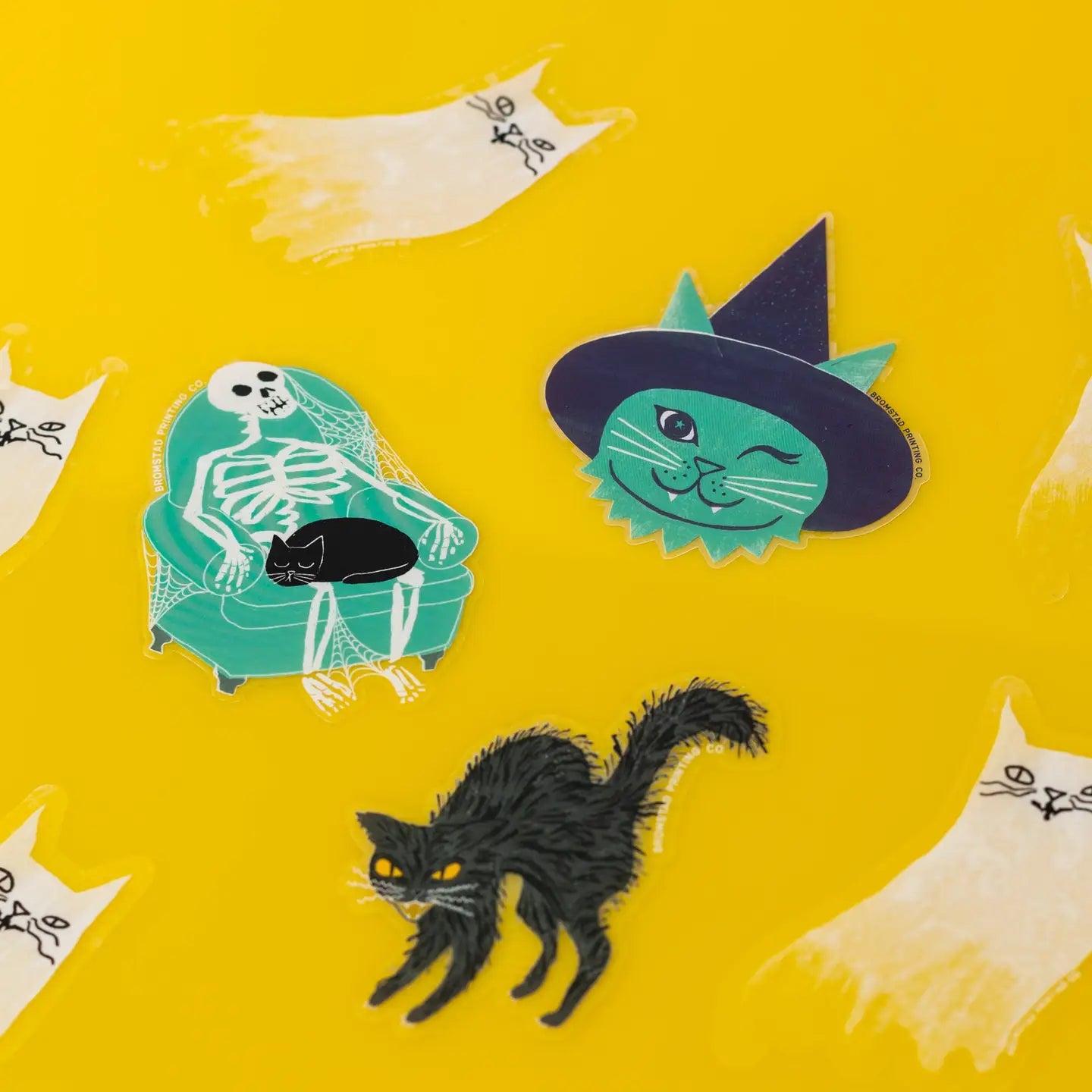 Halloween stickers: knipogende groene kattenheks, skelet in een groenblauwe stoel en slordige zwarte kat op een gele achtergrond.
