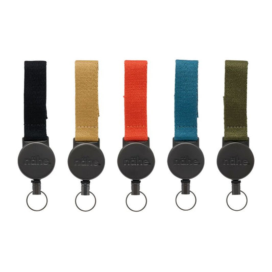 Zwarte Nähe intrekbare sleutelhanger met een stoffen band, een ronde behuizing met reliëf en een metalen sleutelring.