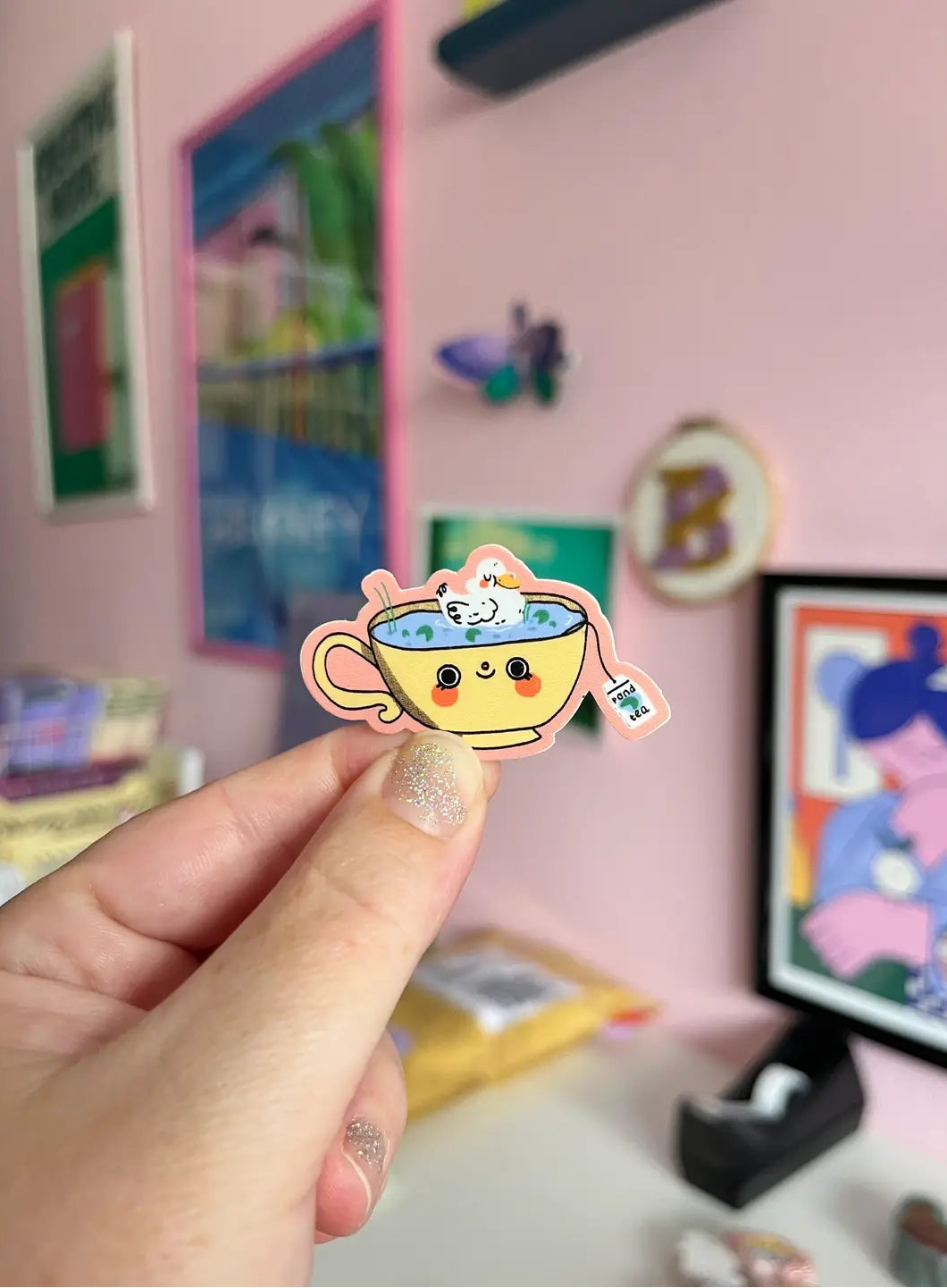Bloemkolie Teatime Duck sticker: schattige witte eend in een lachende gele theekop met blauwe vijverthee en roze rand.
