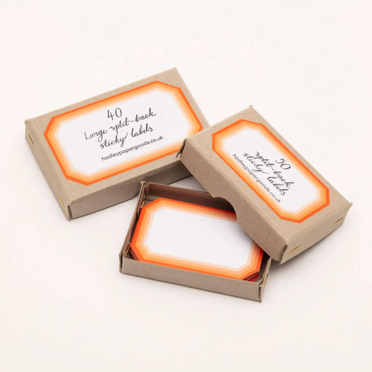 White octagonal stickers with retro tiered orange borders, packaged in small brown cardboard boxes by Hadley.