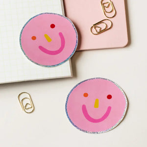 Claire Paul roze ronde stickers met een zilveren holografische rand en een kleurrijke minimalistische smiley.